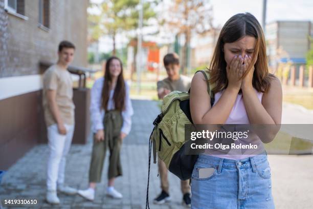 school bullying. crying girl with laughing teenagers behind her at school yard - bullying stock pictures, royalty-free photos & images