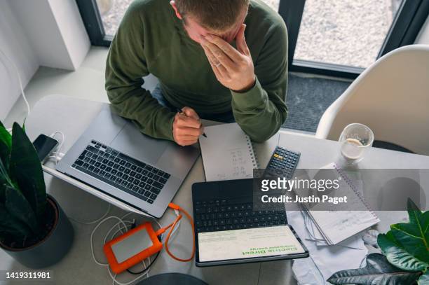 a stressed mature man goes through his home finances at the dining table. - price calculator stock pictures, royalty-free photos & images
