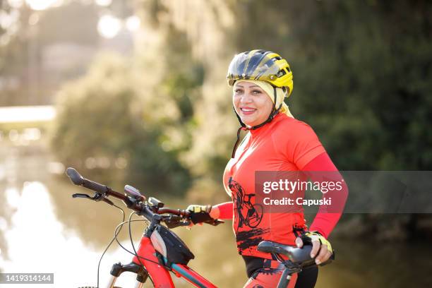 youthful woman in active wear and helmet smiling while holding her bike - only mature women stock pictures, royalty-free photos & images