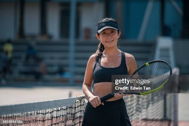 portrait confidence asian chinese female tennis player standing beside tennis net at hardcourt after practise in weekend morning looking at camera smiling - hardcourt stock pictures, royalty-free photos & images