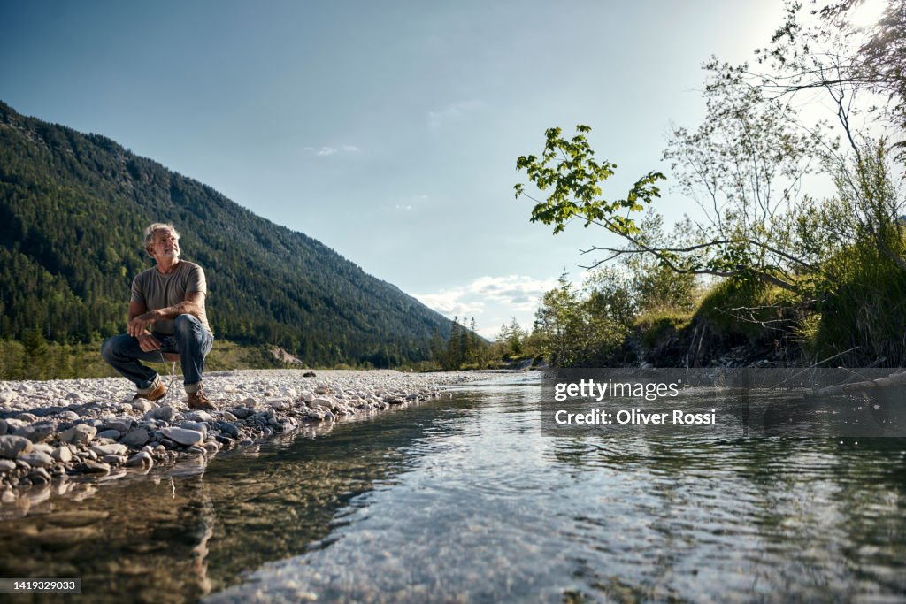 Mature man squatting at a riverbank