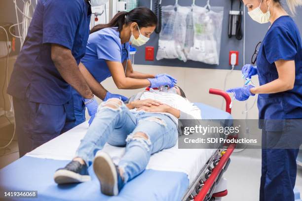 nurse administers oxygen while team prepares to evaluate patient's injuries - doctor emergency imagens e fotografias de stock