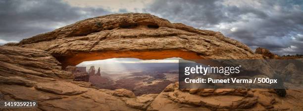 view of rock formations against cloudy sky,mesa arch,united states,usa - mesa arch stockfoto's en -beelden