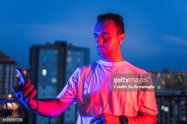 portrait of young man using wireless headphones and smart phone under neon lights - facebook ads stock pictures, royalty-free photos & images