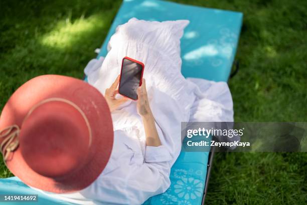 woman using smartphone on sunbed - tuinscherm stockfoto's en -beelden