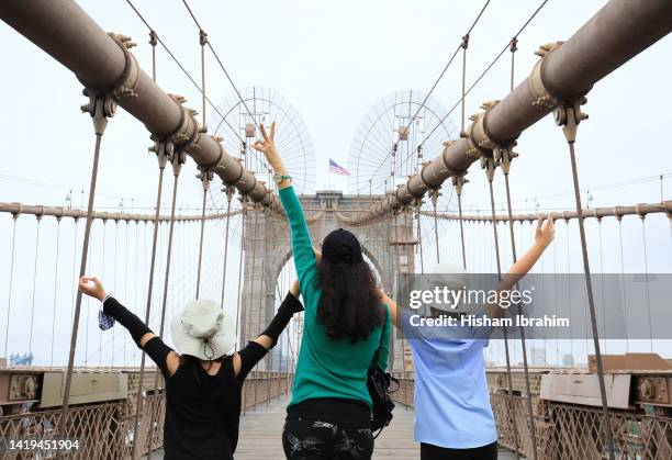 mother and two young daughters loving being on the brooklyn bridge - manhattan, new york city. - touristen brooklyn bridge stock-fotos und bilder