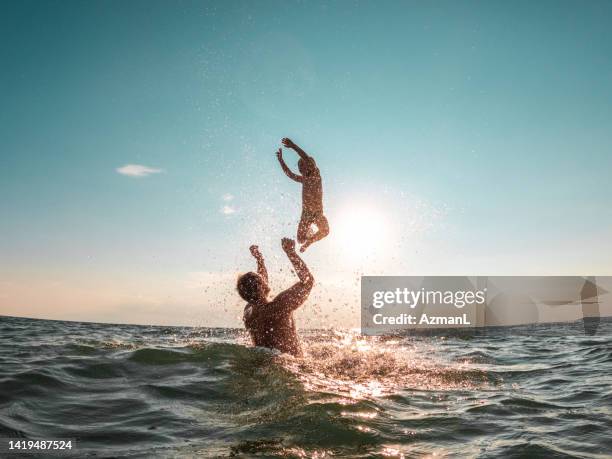 small kid jumping in the air while playing with is father at the beach - jump joy stock pictures, royalty-free photos & images