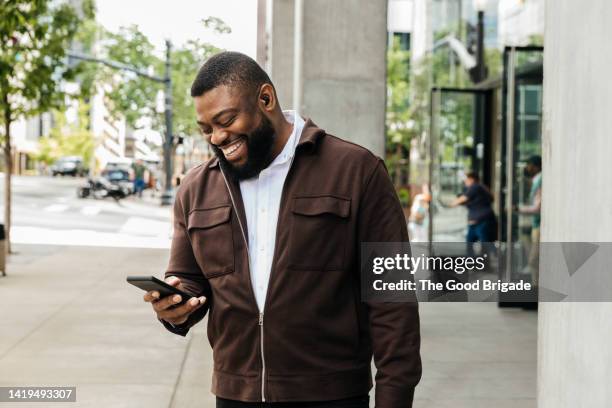 smiling businessman talking on smart phone on city street - ohrhörer stock-fotos und bilder