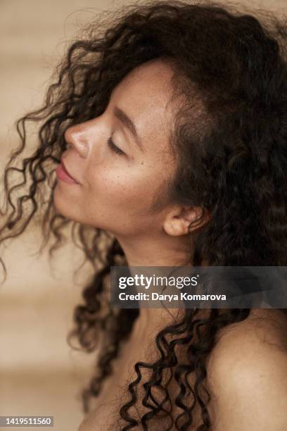 closeup portrait of beautiful young woman with curly hair style and closed eyes on beige background. the woman has smile and freckles. the mulatto in profile is a representative of a mixed race, an african american and a white race. - woman smiling eyes closed stock pictures, royalty-free photos & images