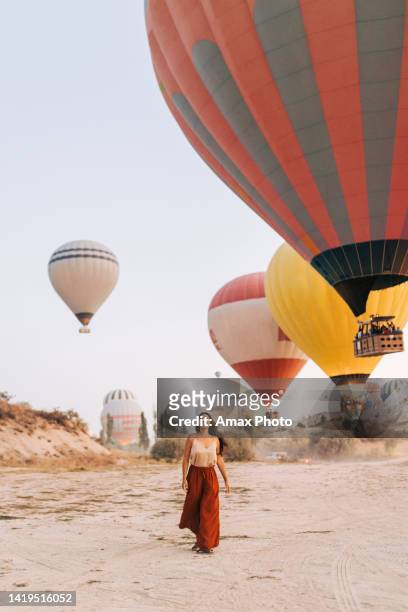 young woman is walking and smiling near hot air balloons in cappadocia - cappadocia hot air balloon stock pictures, royalty-free photos & images