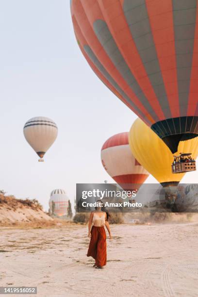 young woman is walking and smiling near hot air balloons in cappadocia - capadócia imagens e fotografias de stock