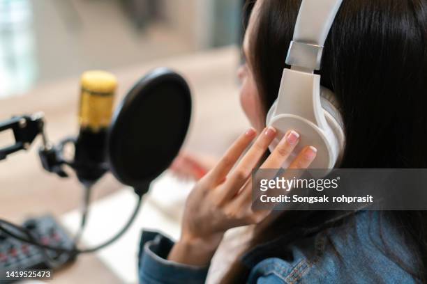 close up of young asian businesswoman recording and broadcasting a podcast on her laptop from studio office. - media equipment stock pictures, royalty-free photos & images