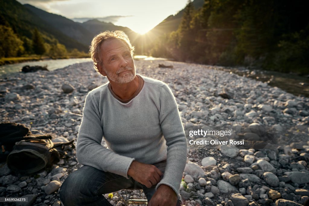 Mature man resting at a riverbank at sunset