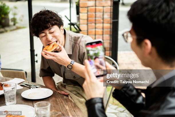 a man has a friend take a picture of him eating pizza on vacation with his smartphone. - asian man stockfoto's en -beelden