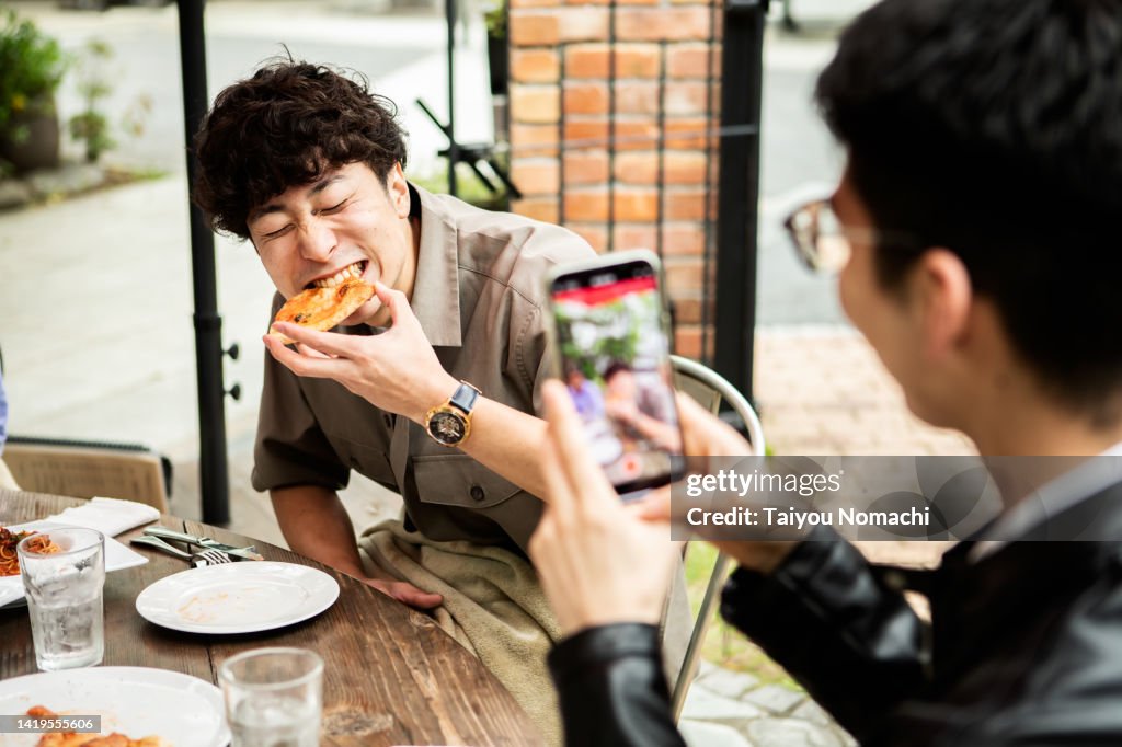 A man has a friend take a picture of him eating pizza on vacation with his smartphone.