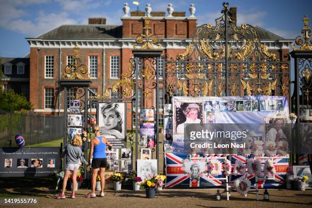 Two people stop to look at the messages and photographs outside Kensington Palace as fans of Princess Diana gather to show their support on August...