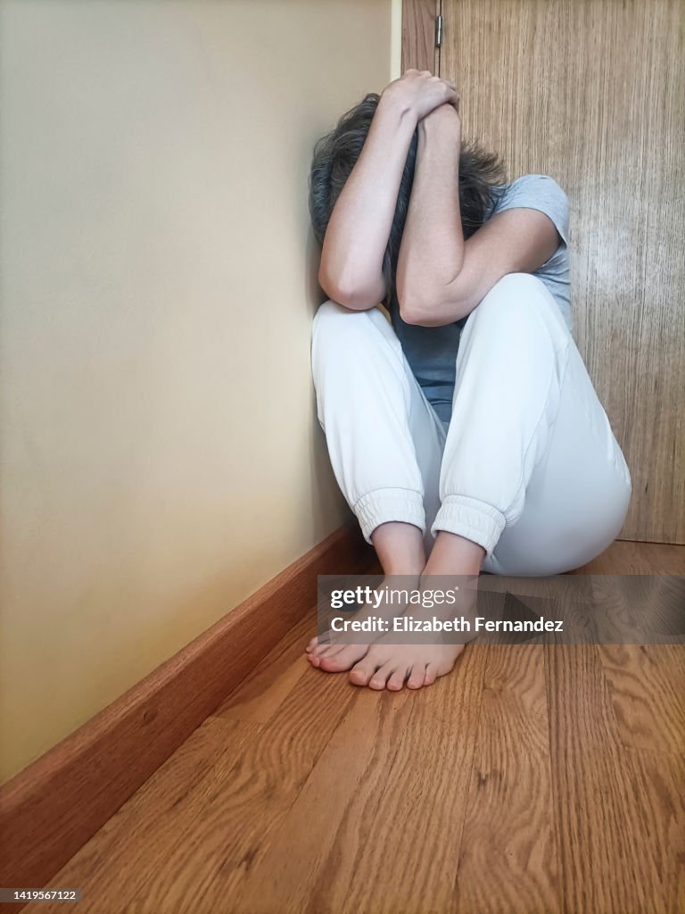 Unhappy and depressed woman sitting on room floor, hides her face.