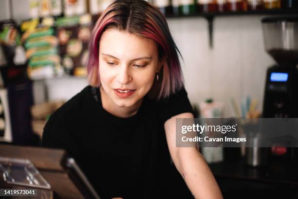 happy young female barista working at checkout counter in coffee shop - hipster coffee shop candid stock-fotos und bilder