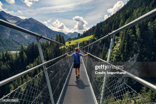 mutter und sohn im teenageralter wandern auf einer hängebrücke in den österreichischen bergen - alpen, tirol, österreich. - valley side stock-fotos und bilder