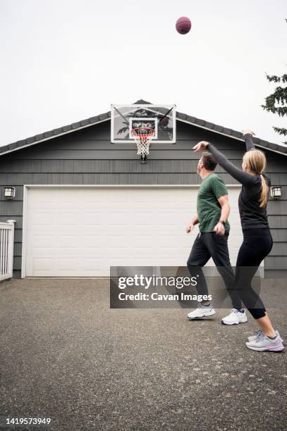 father and teen girl shooting baskets in driveway at home - shooting baskets in driveway stock pictures, royalty-free photos & images