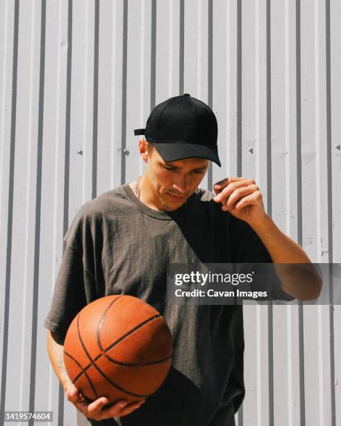 stylish guy in dark clothes and a black cap with a basketball - cap hat stockfoto's en -beelden