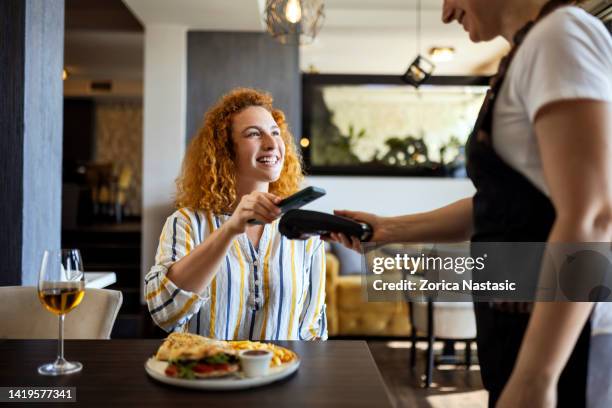 lächelnder junger, der kontaktlos mit dem smartphone bezahlt - bezahlen stock-fotos und bilder
