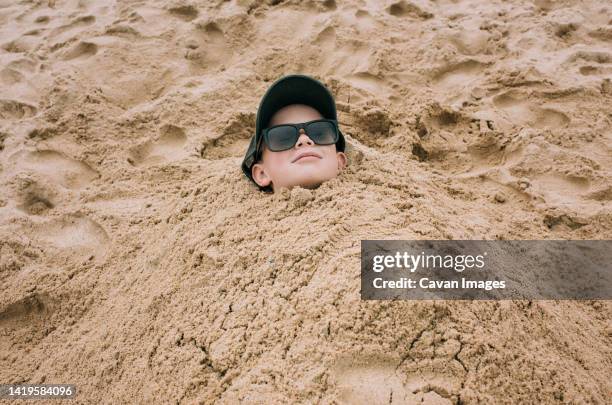 boy burried in sand relaxing happily at the beach - buried in sand stockfoto's en -beelden