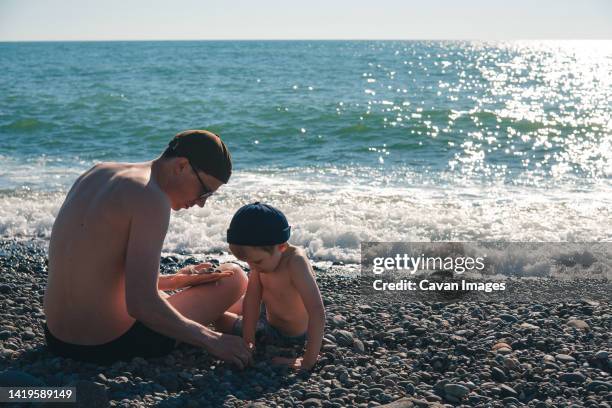 a little boy and his father sit near the sea and play - georgia love fotografías e imágenes de stock