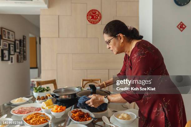 chinese new year - senior indian woman from a multi racial and multi generation family setting the table for reunion dinner - indian food stockfoto's en -beelden