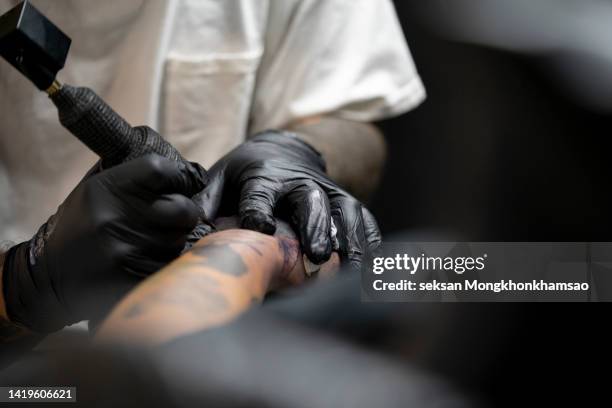 tattooist tattooing young mans arm, close-up - tatuaje fotografías e imágenes de stock