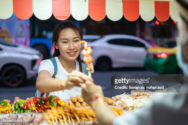 woman buys skewered grilled pork - night market stock-fotos und bilder