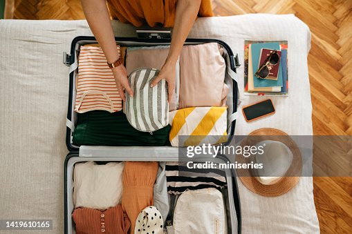 Beschnittenes Foto einer unkenntlichen Frau, die eine Kosmetiktasche in ihren Koffer steckt Beschnittenes Foto einer unkenntlichen Frau, die eine Kosmetiktasche in ihren Koffer steckt