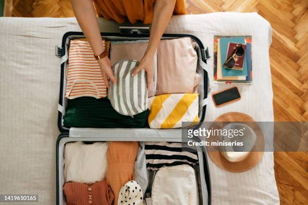 beschnittenes foto einer unkenntlichen frau, die eine kosmetiktasche in ihren koffer steckt - vacation luggage stock-fotos und bilder