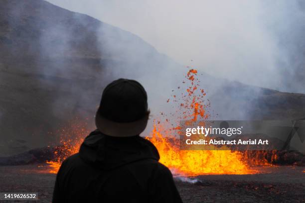 one tourist standing close to an erupting volcano, iceland - grindavik stock-fotos und bilder