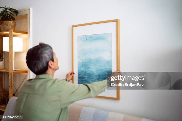 woman decorating her home with a new painting - hanging art stock pictures, royalty-free photos & images