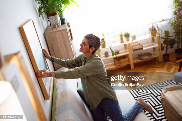 woman decorating her home with a new painting - hanging stock pictures, royalty-free photos & images