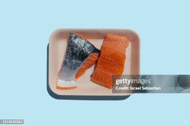 top view image of two pieces of raw salmon in a disposable plastic tray on a blue plain background. with copy space on top. - lachssteak stock-fotos und bilder