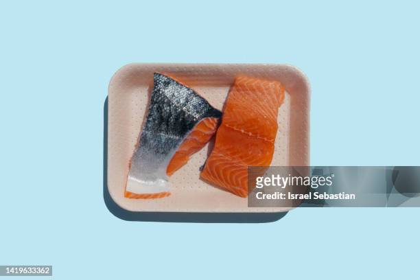 top view image of two pieces of raw salmon in a disposable plastic tray on a blue plain background. with copy space on top. - salmon steak stockfoto's en -beelden