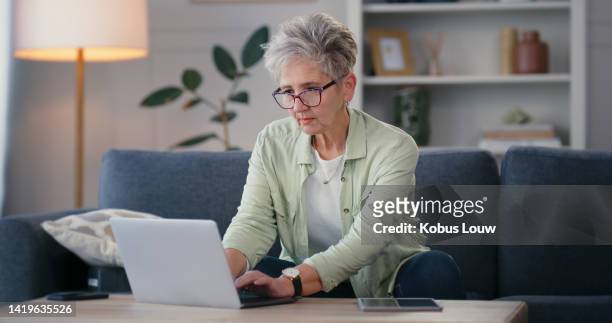 online shopping, social media or ecommerce, a senior woman working on laptop on a sofa at home. an elderly lady with internet connection checking a computer for email from family, friends or business - modern family media call stockfoto's en -beelden