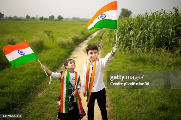 enfants d’âge élémentaire debout près d’un champ vert tenant le drapeau indien national dans les mains. - republic day photos et images de collection
