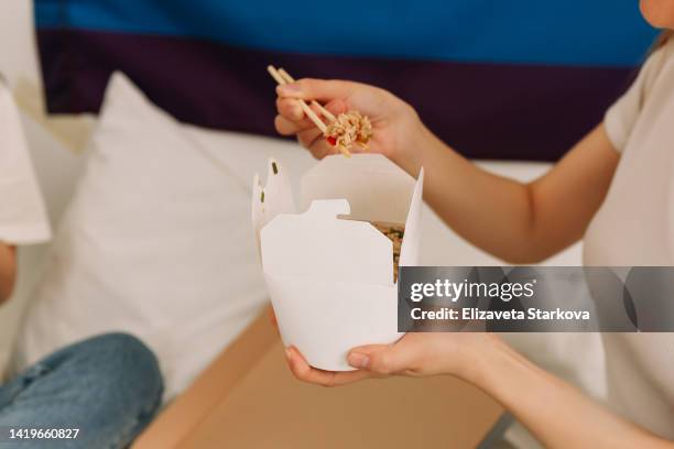 close-up of human hands holding a box of chinese food noodles and chinese chopsticks at home. food delivery - chinese takeaway stock pictures, royalty-free photos & images