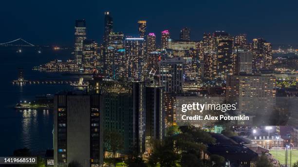 jersey city night view from hoboken with illuminated stadium at the front, and verrazzano-narrows bridge at the distance. - hoboken stock pictures, royalty-free photos & images