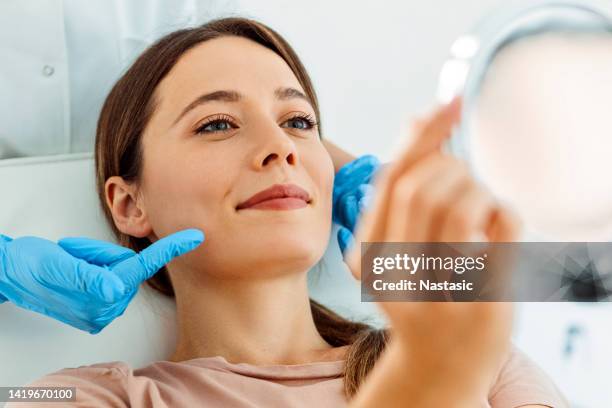 hermosa mujer sonriente que se somete a un tratamiento facial mirándose al espejo - botox fotografías e imágenes de stock