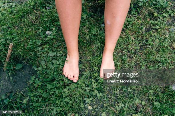 wet bare feet of a teenager girl standing on the green grass by the river during the rain. the concept of unity with nature, rational use of natural resources, sustainability, zero waste - womans bare feet fotografías e imágenes de stock