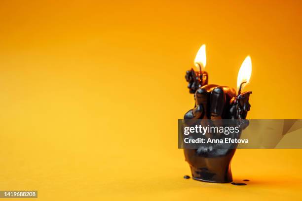 black burning soy or wax candle in shape of a hand doing the horn sign on yellow background. concept of halloween celebration. perfect backdrop for your design with copy space - rock music background stock pictures, royalty-free photos & images