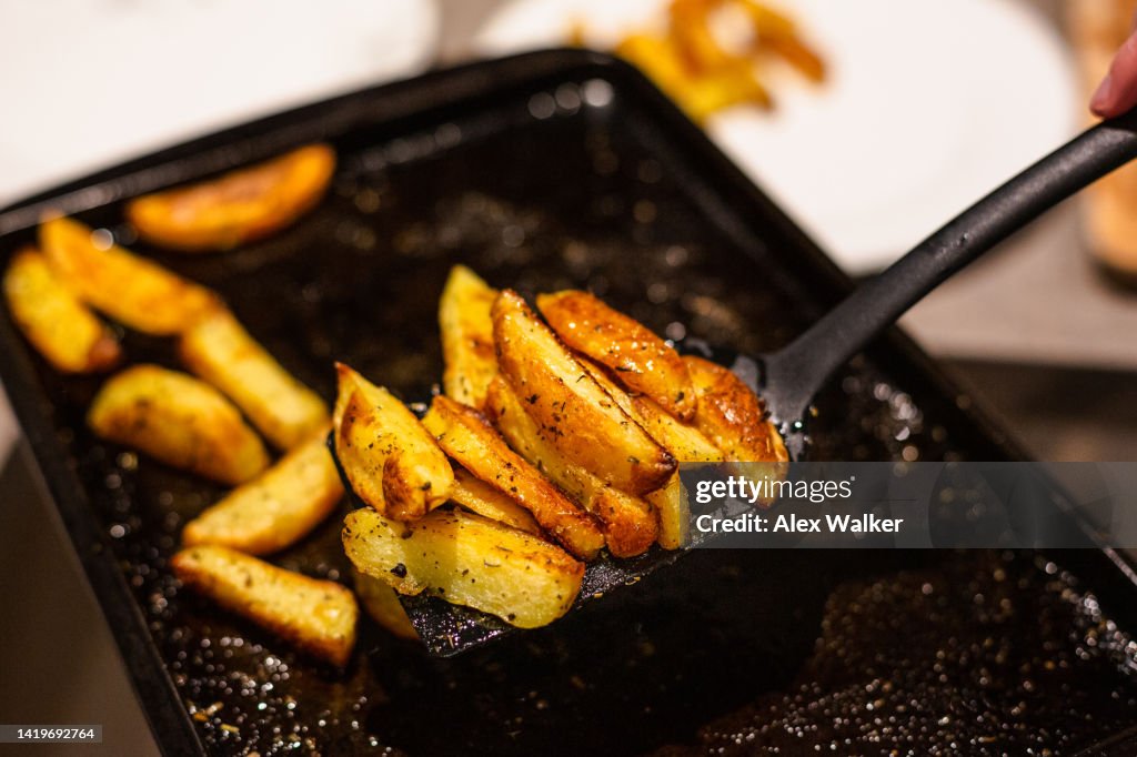 Seasoned potato wedges on baking tray with spatula