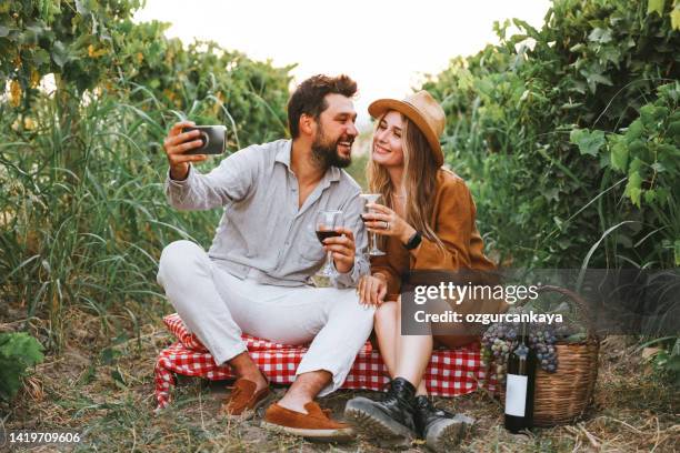 couple clinking red wine glass in a vineyard during sunset. - wine tasting online stock pictures, royalty-free photos & images