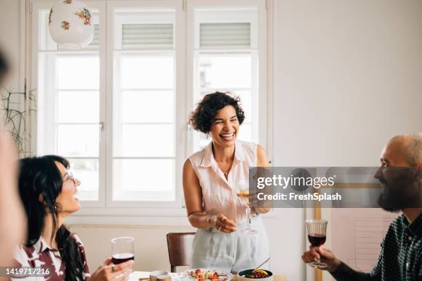 a beautiful happy woman standing and making a toast while holding a glass of champagne - hostesses stockfoto's en -beelden