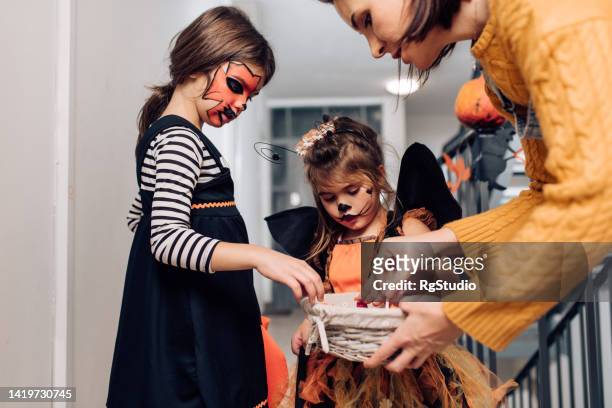 süße mädchen in halloween-kostümen sammeln süßigkeiten in der nachbarschaft - halloween candy stock-fotos und bilder