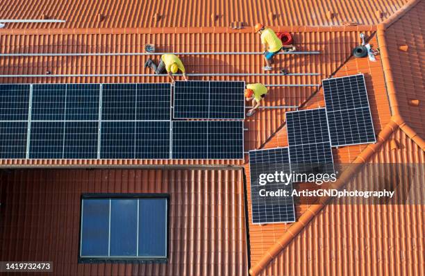 shot from above of a team of professional workers installing solar panels system on a roof. - solar farm stock pictures, royalty-free photos & images